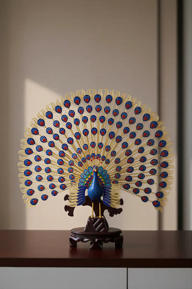 Handcrafted Chinese Cloisonné peacock sculpture featuring intricate gold filigree tail feathers and vibrant blue enamel body, displayed on a dark wooden stand.