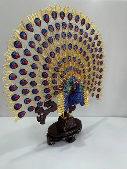 Handcrafted Cloisonné peacock statue with an intricate golden filigree tail and vibrant blue enamel body, symbolizing eternal grace and prosperity, displayed on a carved wooden base.